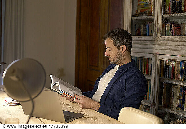 Businessman reading book at desk in home office
