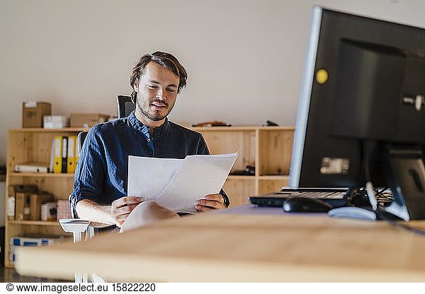Businessman reading document at desk in wooden open-plan office