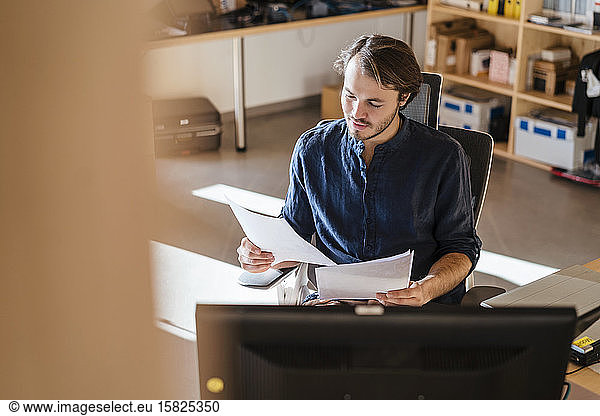 Businessman reading document at desk in wooden open-plan office