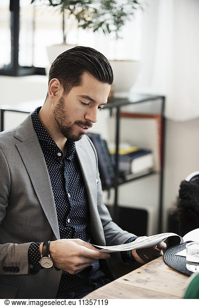 Businessman reading document while sitting at table in office