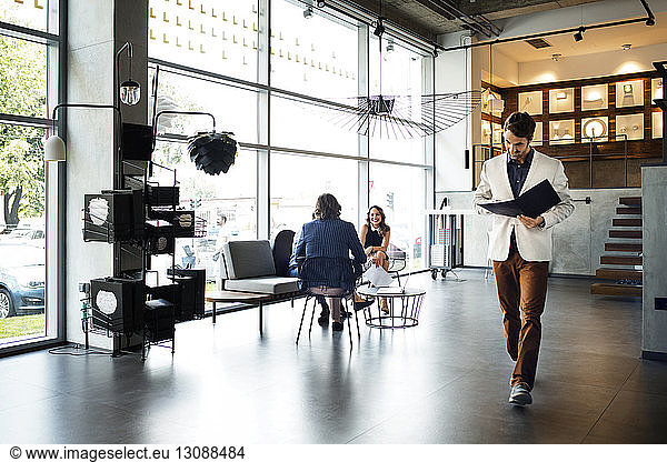 Businessman reading file while walking in office by colleagues in background