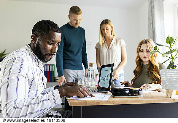 Businessman reading paper document on desk by colleagues at workplace