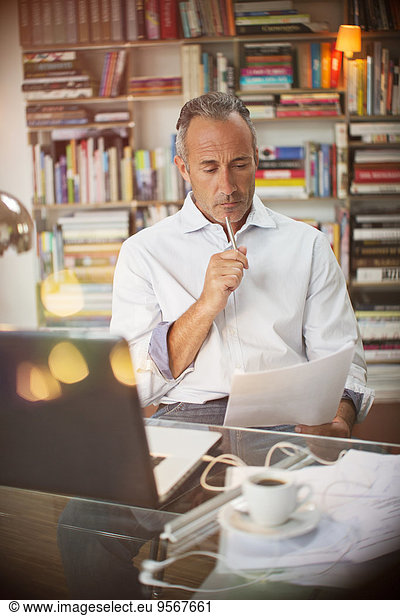 Businessman reading paperwork at home office desk