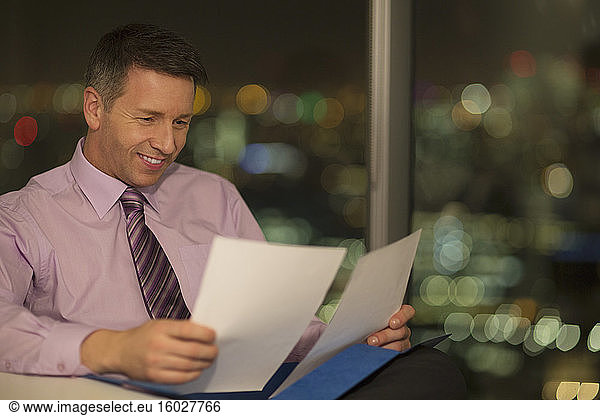 Businessman reading paperwork in office at night