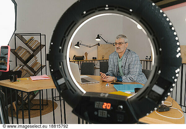 Businessman recording online class in studio seen through ringlight