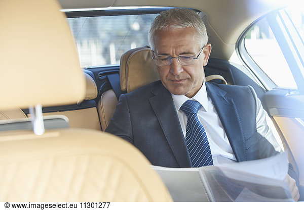 Businessman reviewing paperwork in back seat of town car