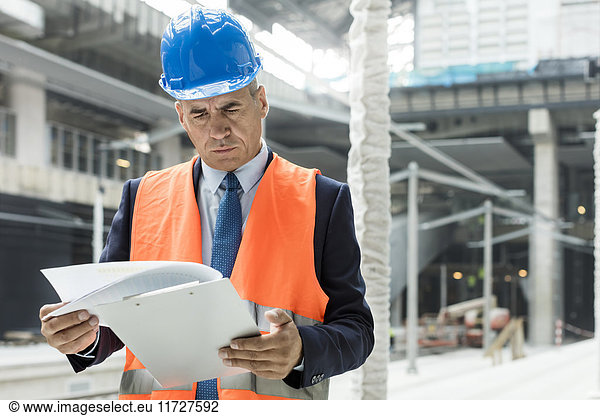 Businessman reviewing paperwork on clipboard at construction site