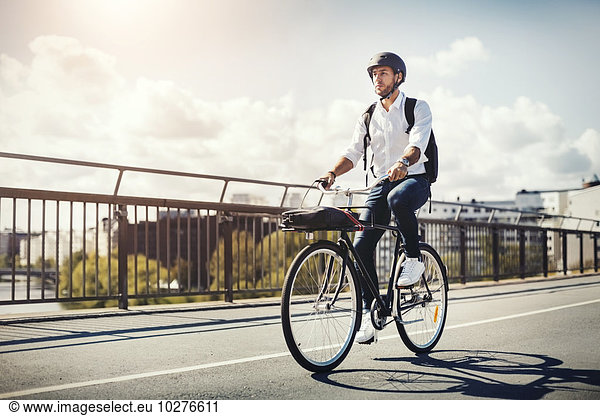 Businessman riding bicycle on bridge against sky