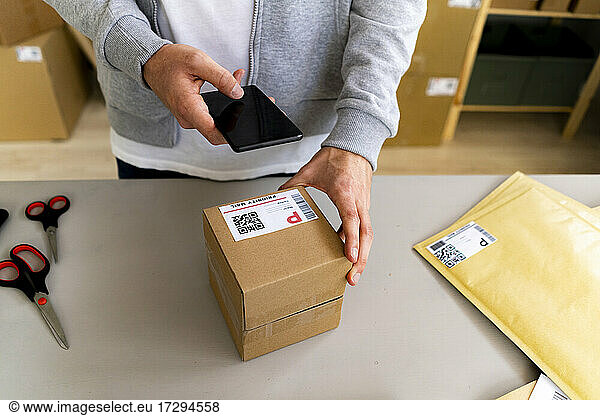 Businessman scanning QR code on box through smart phone at desk