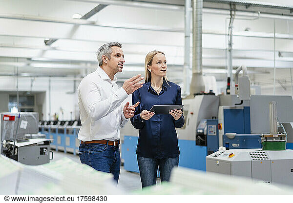 Businessman sharing ideas with businesswoman holding tablet PC in factory