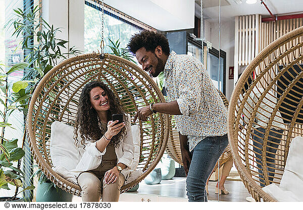 Businessman sharing mobile phone with businesswoman sitting in hanging chair