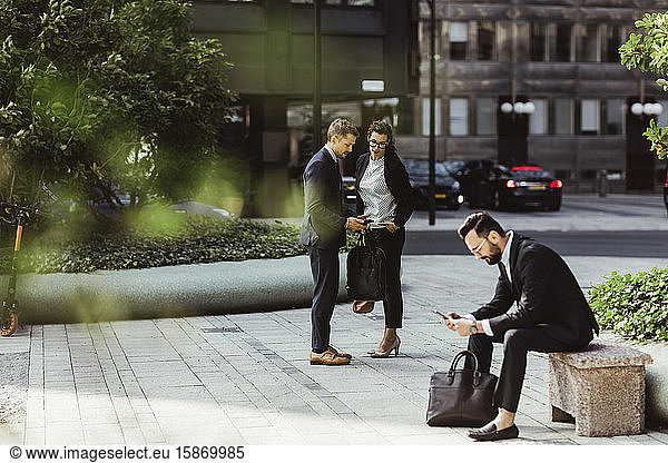 Businessman showing smart phone to female colleague while male coworker surfing net outdoors