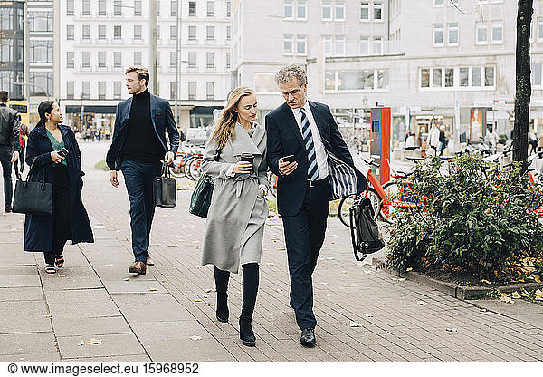Businessman showing smart phone to female colleague while walking in city