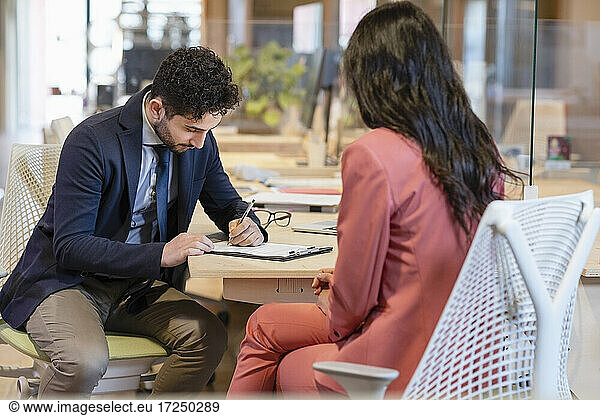 Businessman signing contract in front of female professional in office