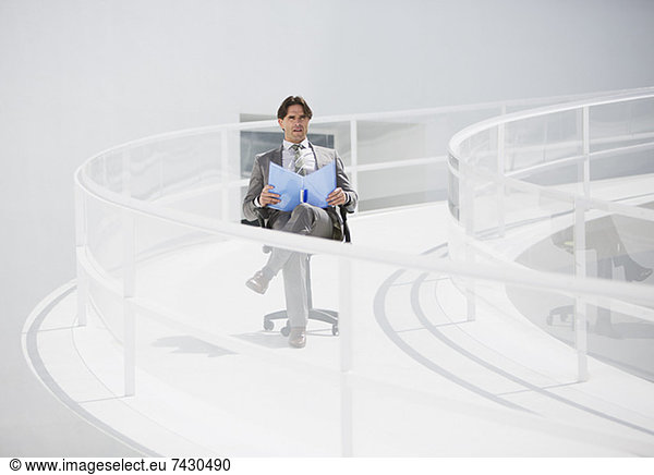 Businessman sitting in chair with folder on elevated walkway