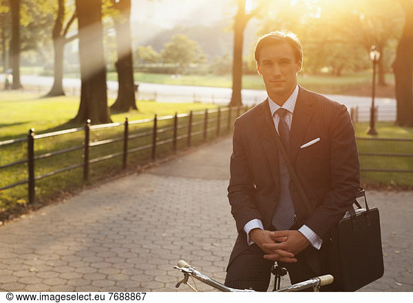 Businessman sitting on bicycle in urban park