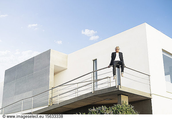 Businessman sitting on handrail in front of his modern house