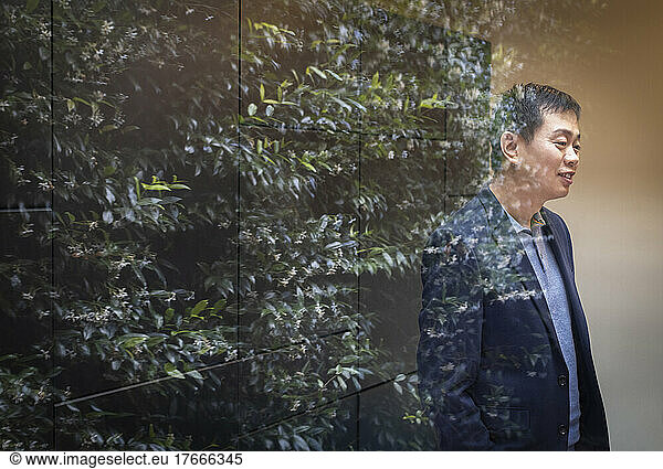 Businessman standing at window with reflection of tree