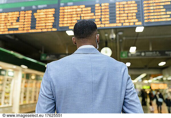 Businessman standing in front of departure board at train station