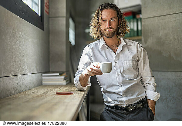 Businessman standing in office with hand in pocket drinking coffee