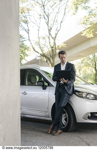 Businessman standing next to car using laptop