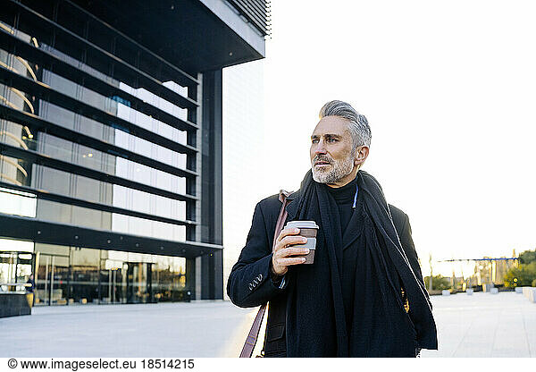 Businessman standing with coffee cup on footpath at sunset