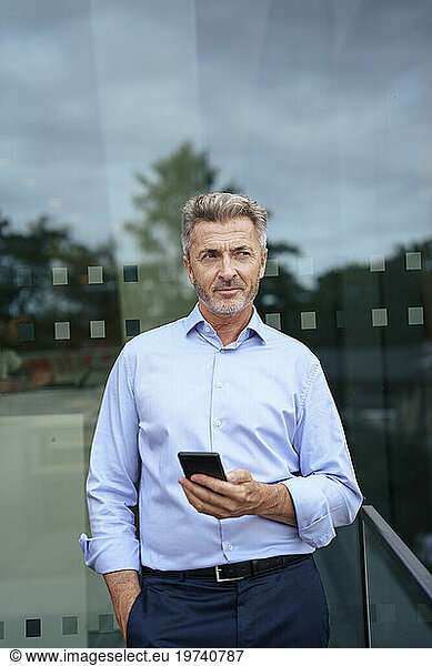 Businessman standing with mobile phone in front of glass