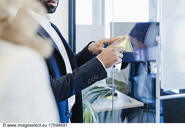 Businessman sticking adhesive note on glass at office