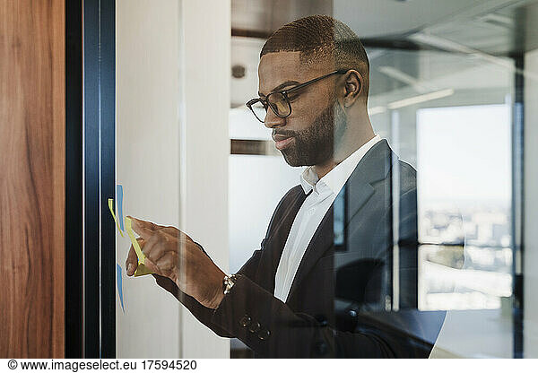 Businessman sticking adhesive note on glass wall at office