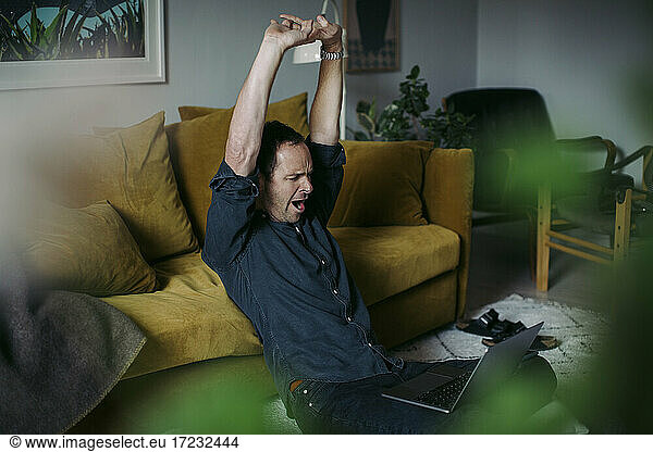 Businessman stretching hands while sitting with laptop in living room