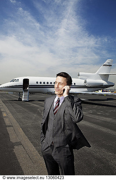 Businessman talking on phone while standing against corporate jet on runway