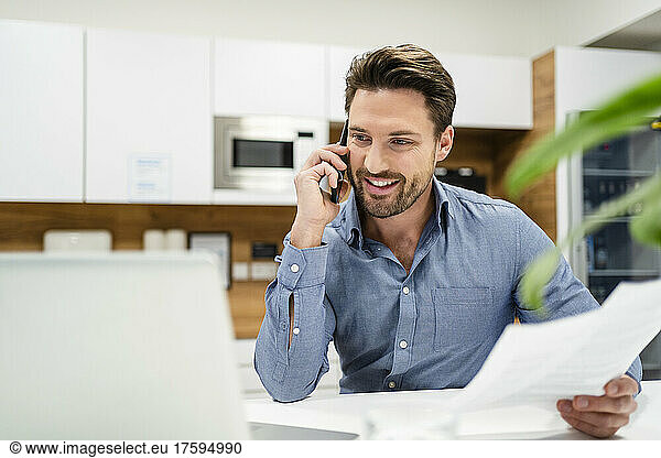 Businessman talking on smart phone and using laptop in office