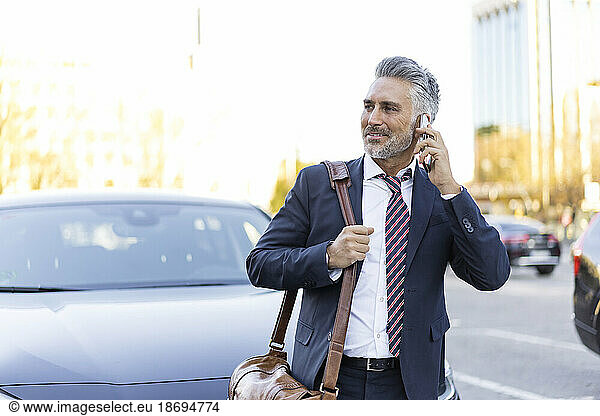 Businessman talking on smart phone standing near car