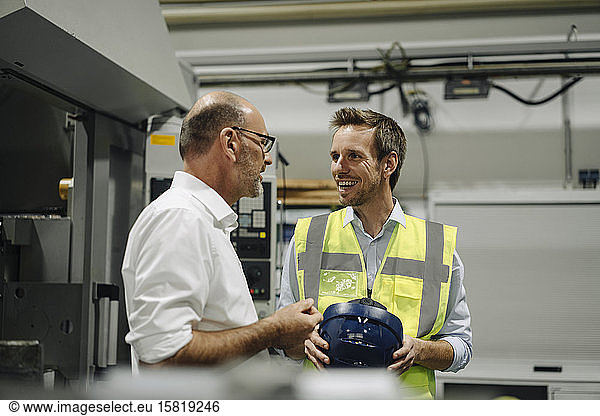 Businessman talking to smiling man in reflective vest in a factory
