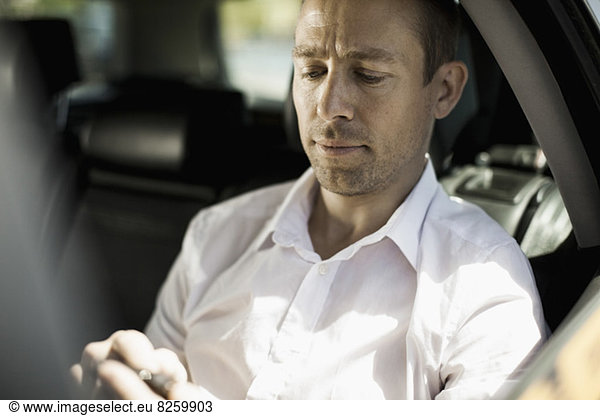 Businessman text messaging through mobile phone in taxi