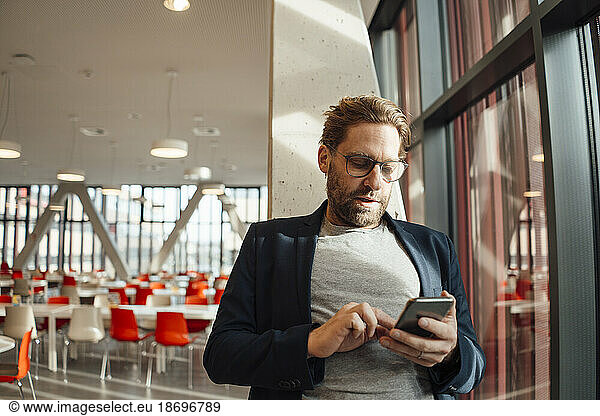 Businessman text messaging through smart phone at cafeteria