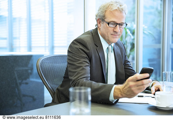 Businessman text messaging with cell phone in conference room