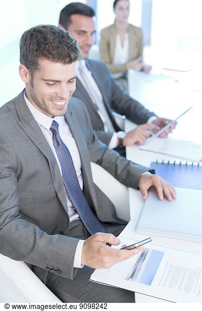 Businessman texting with cell phone in conference room