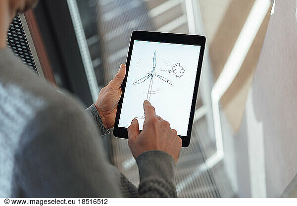 Businessman touching screen of tablet PC with wind turbine drawing in office