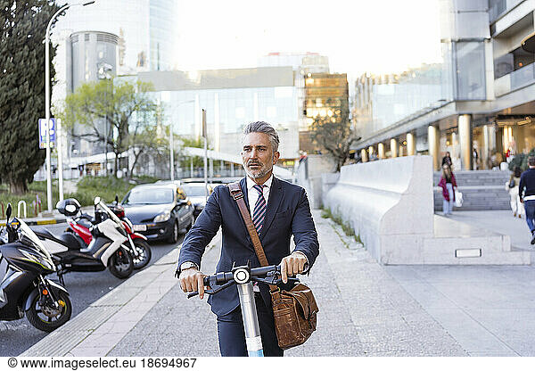 Businessman traveling through electric scooter on sidewalk