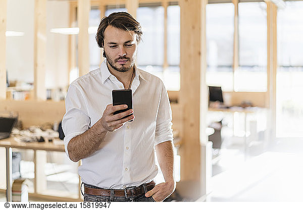 Businessman using cell phone in wooden open-plan office