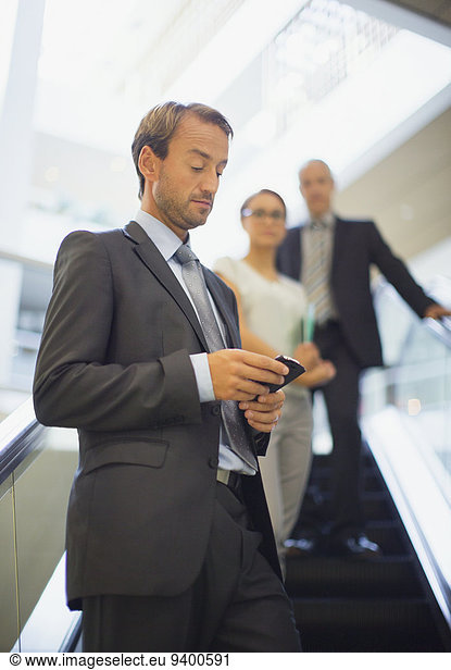 Businessman using cell phone on escalator