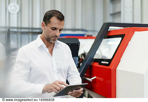 Businessman using digital tablet while standing by machinery at factory
