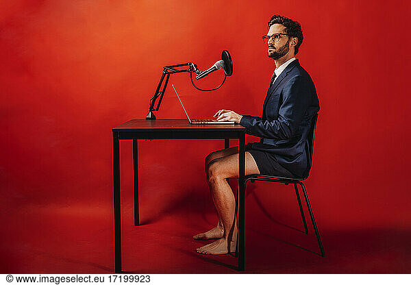 Businessman using laptop at desk by red background