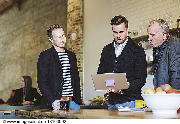 Businessman using laptop computer while standing with male colleagues in office