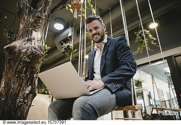 Businessman using laptop in coworking space  sitting on swing