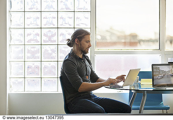 Businessman using laptop on table against window in creative office