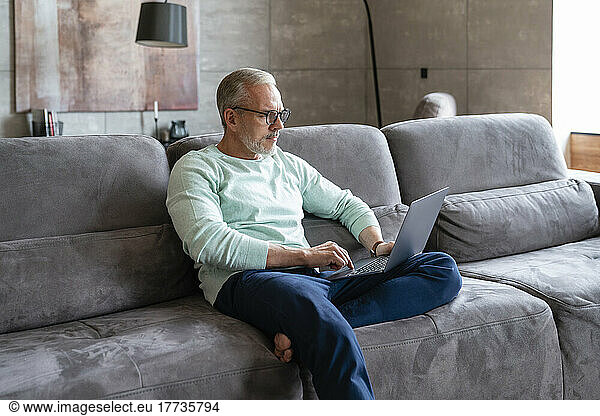 Businessman using laptop sitting on sofa in living room at home