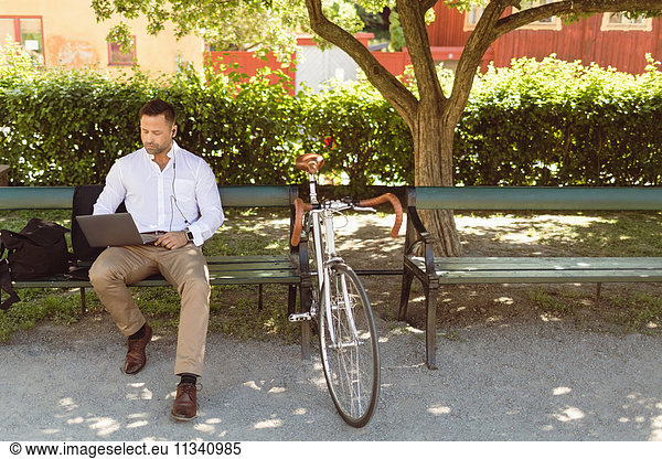 Businessman using laptop while sitting on park bench