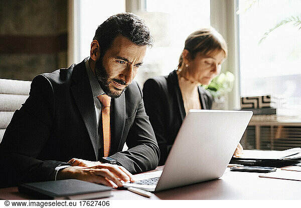 Businessman using laptop working by businesswoman at desk in law office